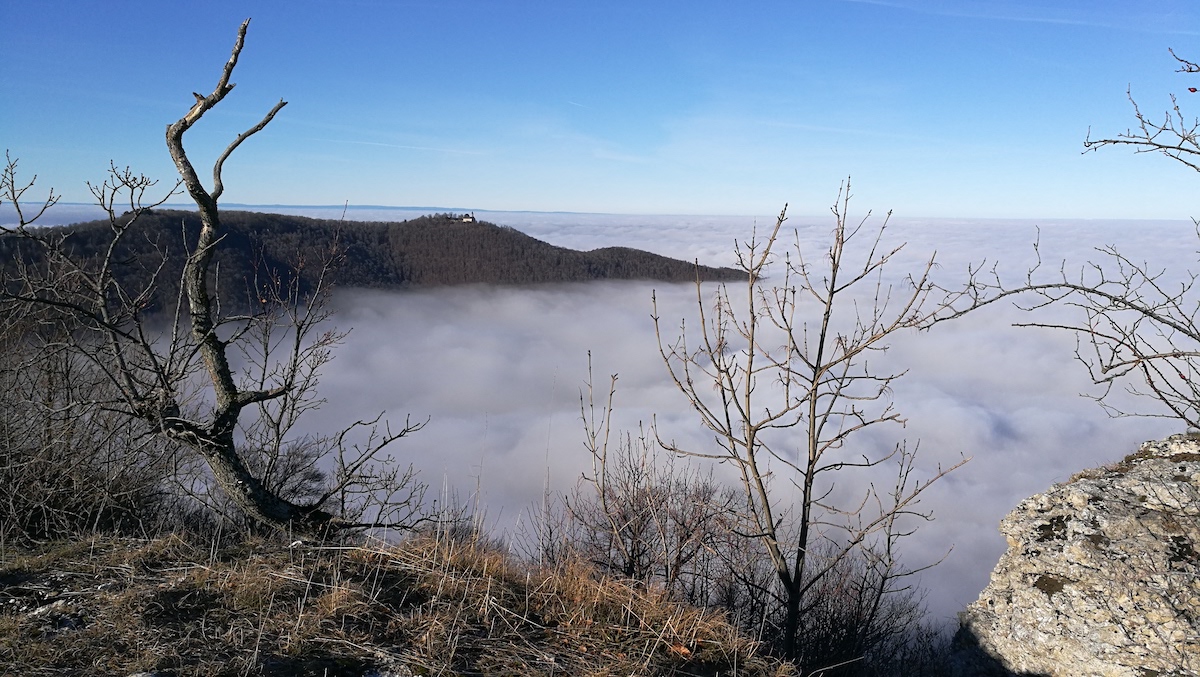 Das Bild zeigt die Aussicht von einem Berg in ein Tal, das gefüllt mit Wochen ist. Der Himmel darüber ist strahlend blau.